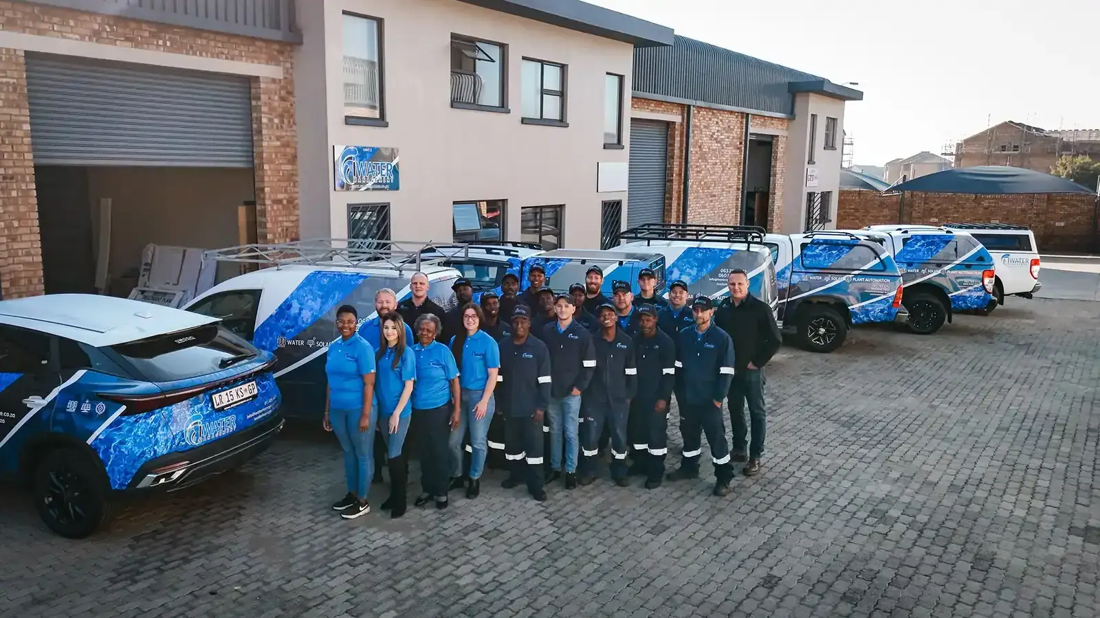 Full iWater team standing with branded vehicles