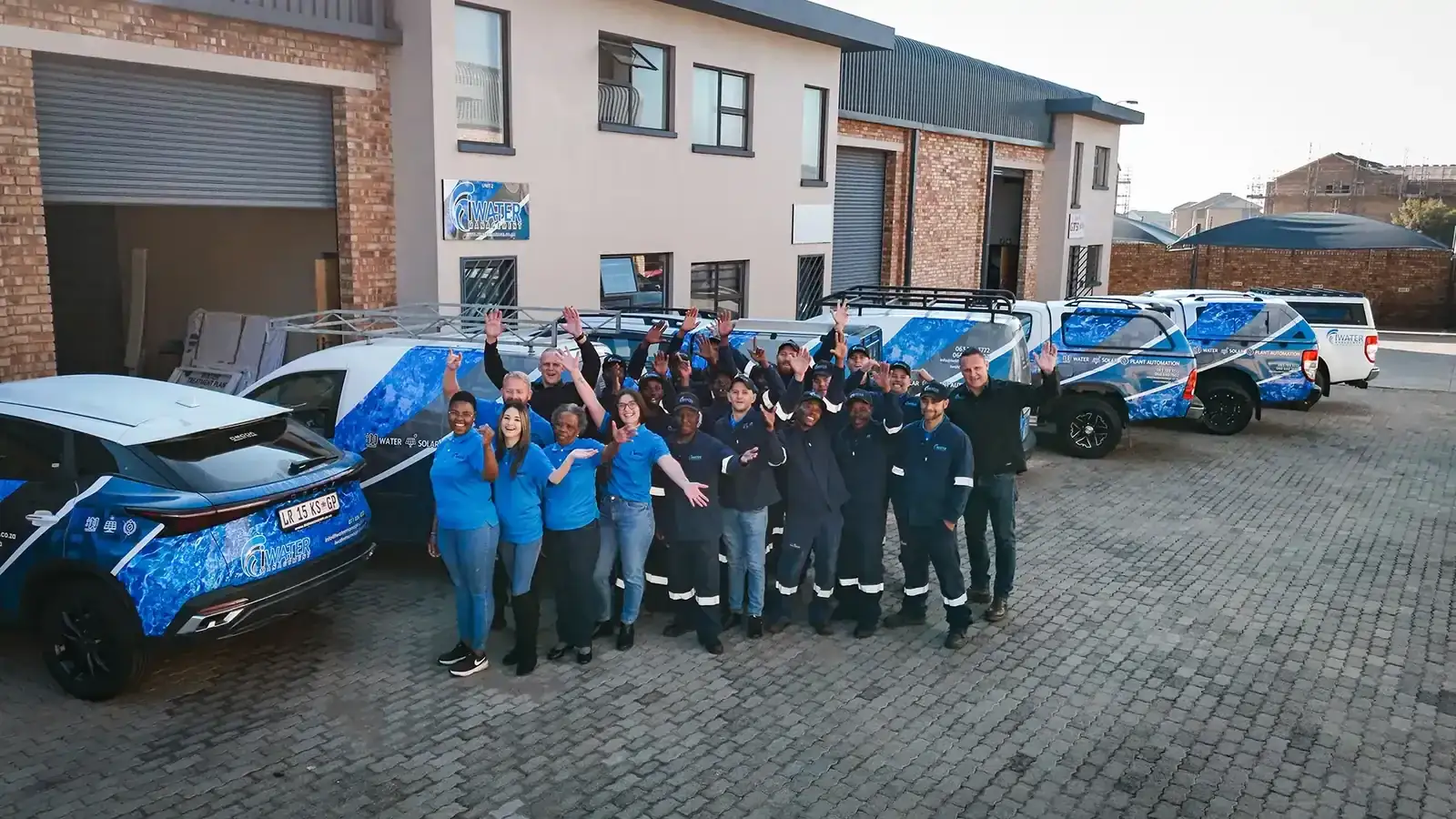 Full iWater team waving with branded vehicles